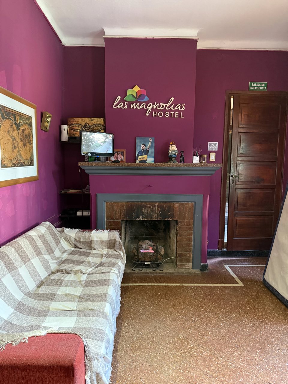 Sala de estar con hogar a leña y el cartel de Las Magnolias Hostel en la pared