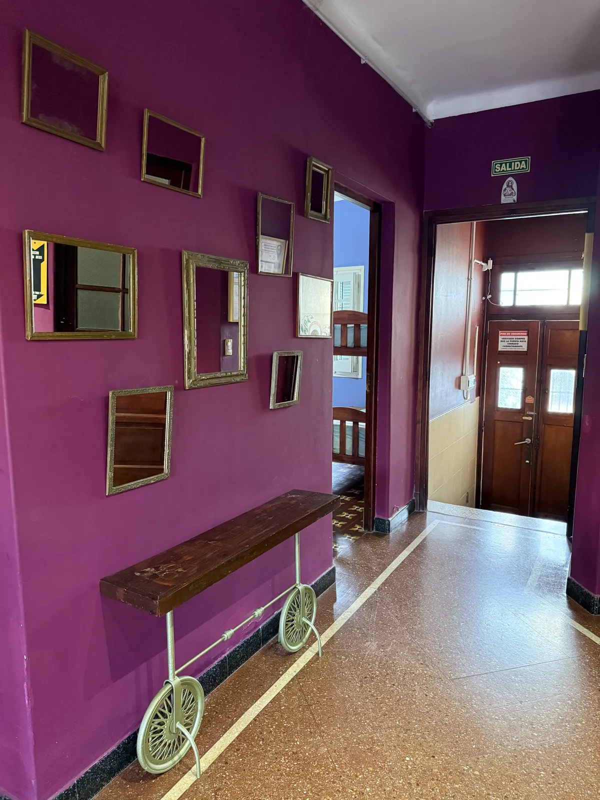 Pasillo fucsia con espejos antiguos y banco de madera que lleva a la puerta de entrada