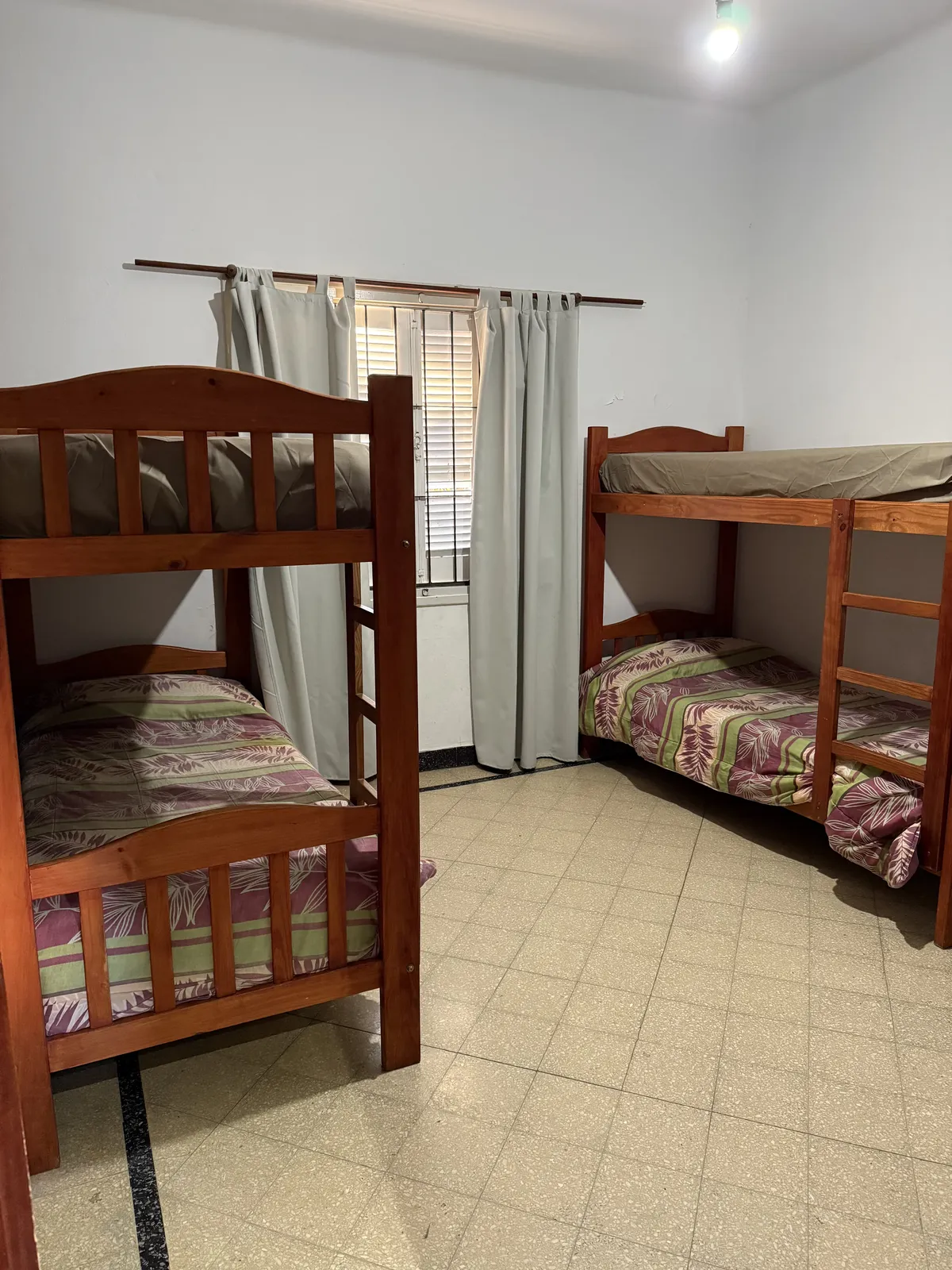 Dormitorio compartido con dos cuchetas de madera y ventana con cortinas