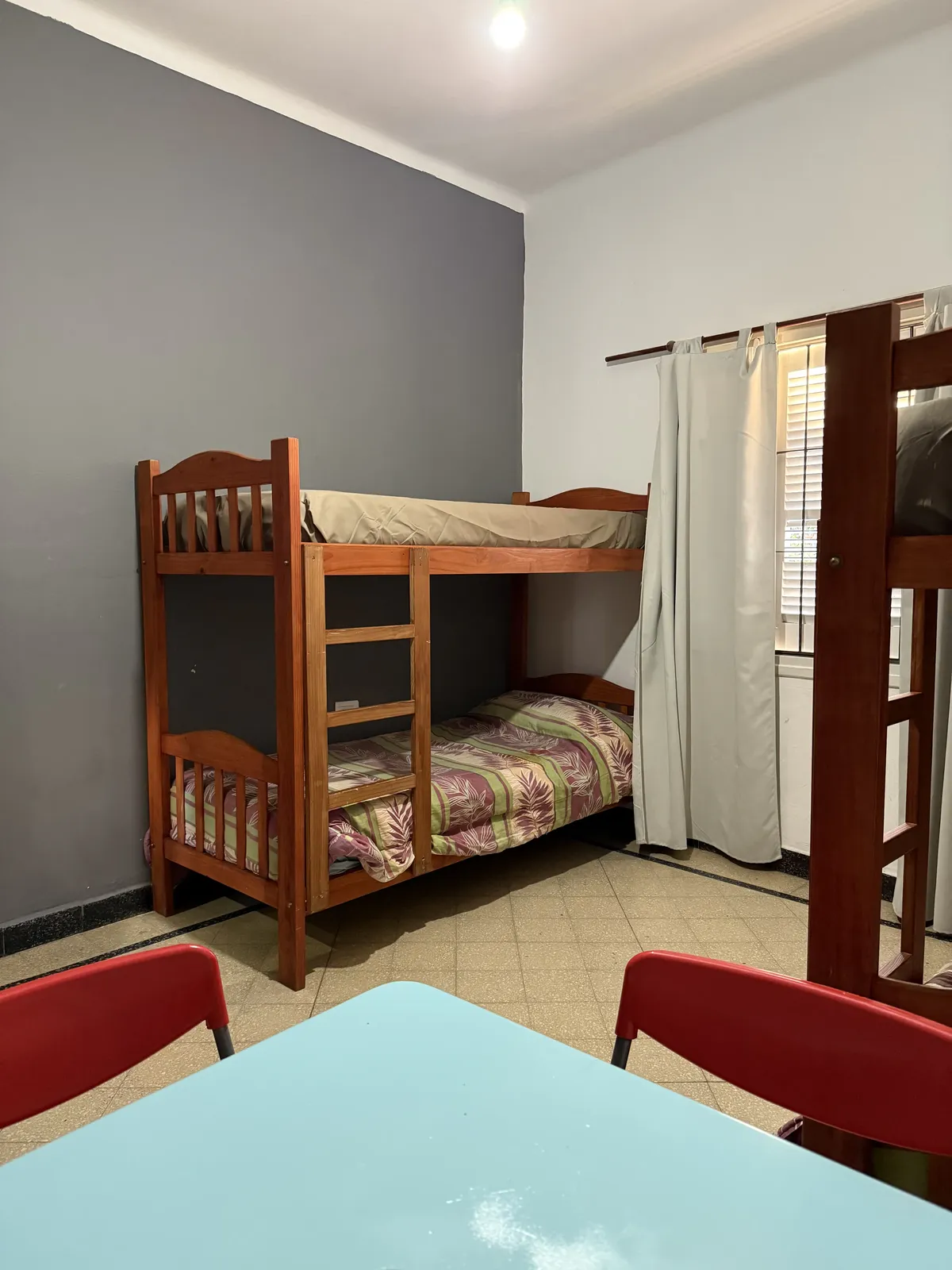 Dormitorio con cucheta de madera, pared gris y mesa con sillas rojas