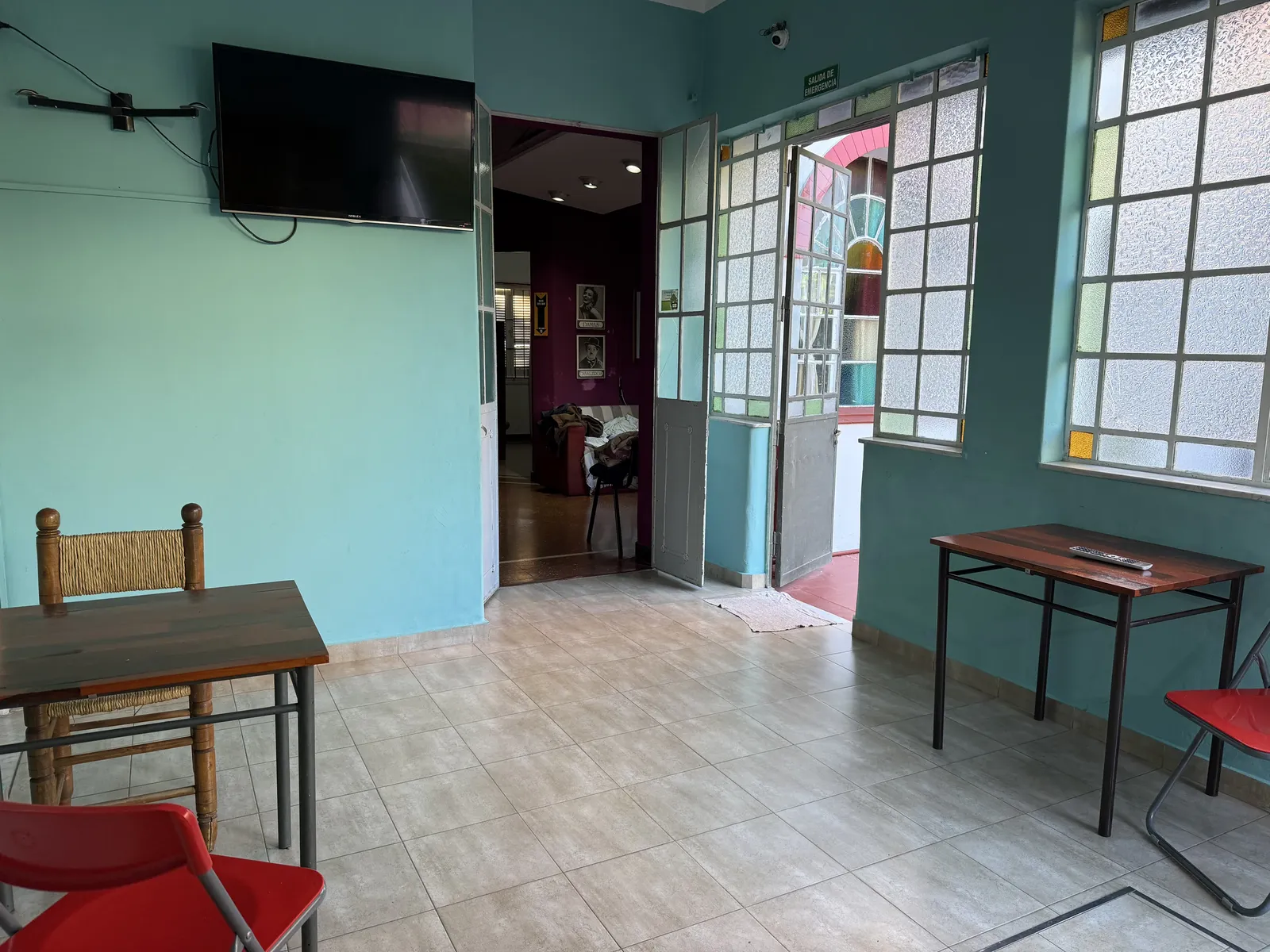Galería interior turquesa con ventanales, televisor y mesas