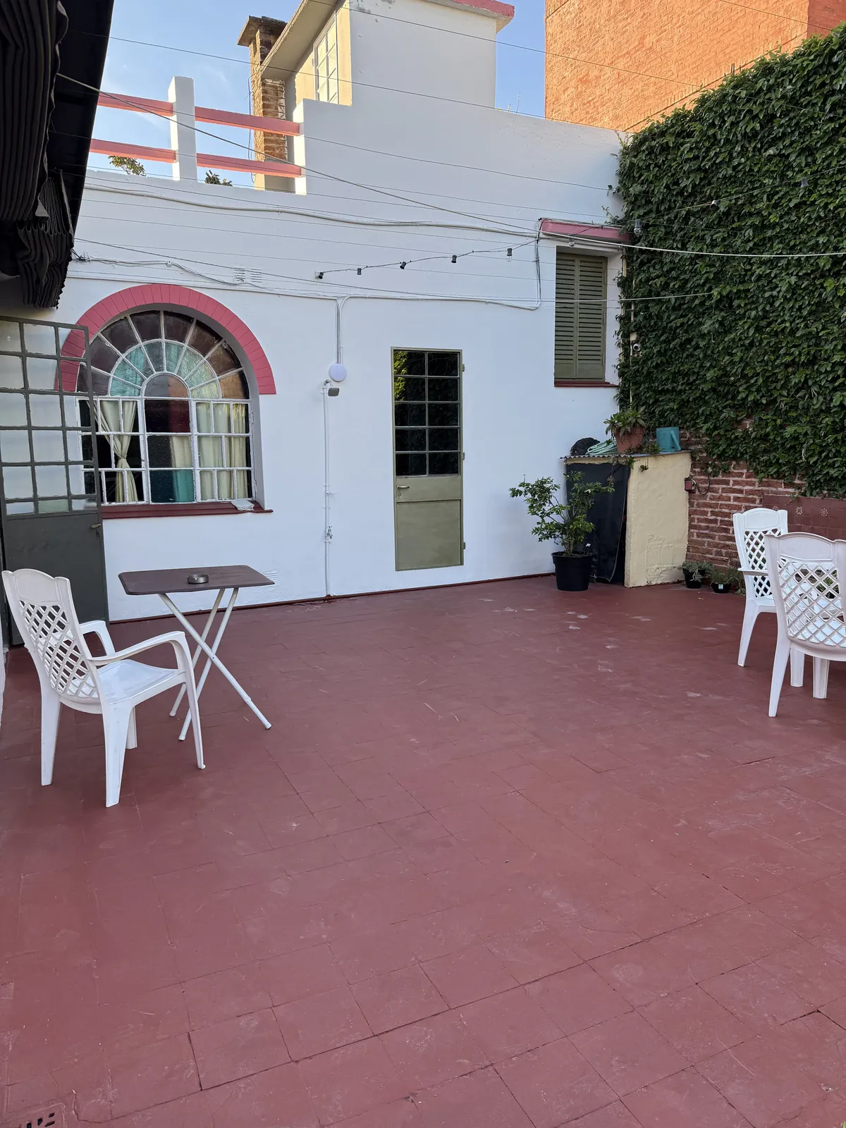Patio con piso rojo, sillas blancas y la casa de fondo