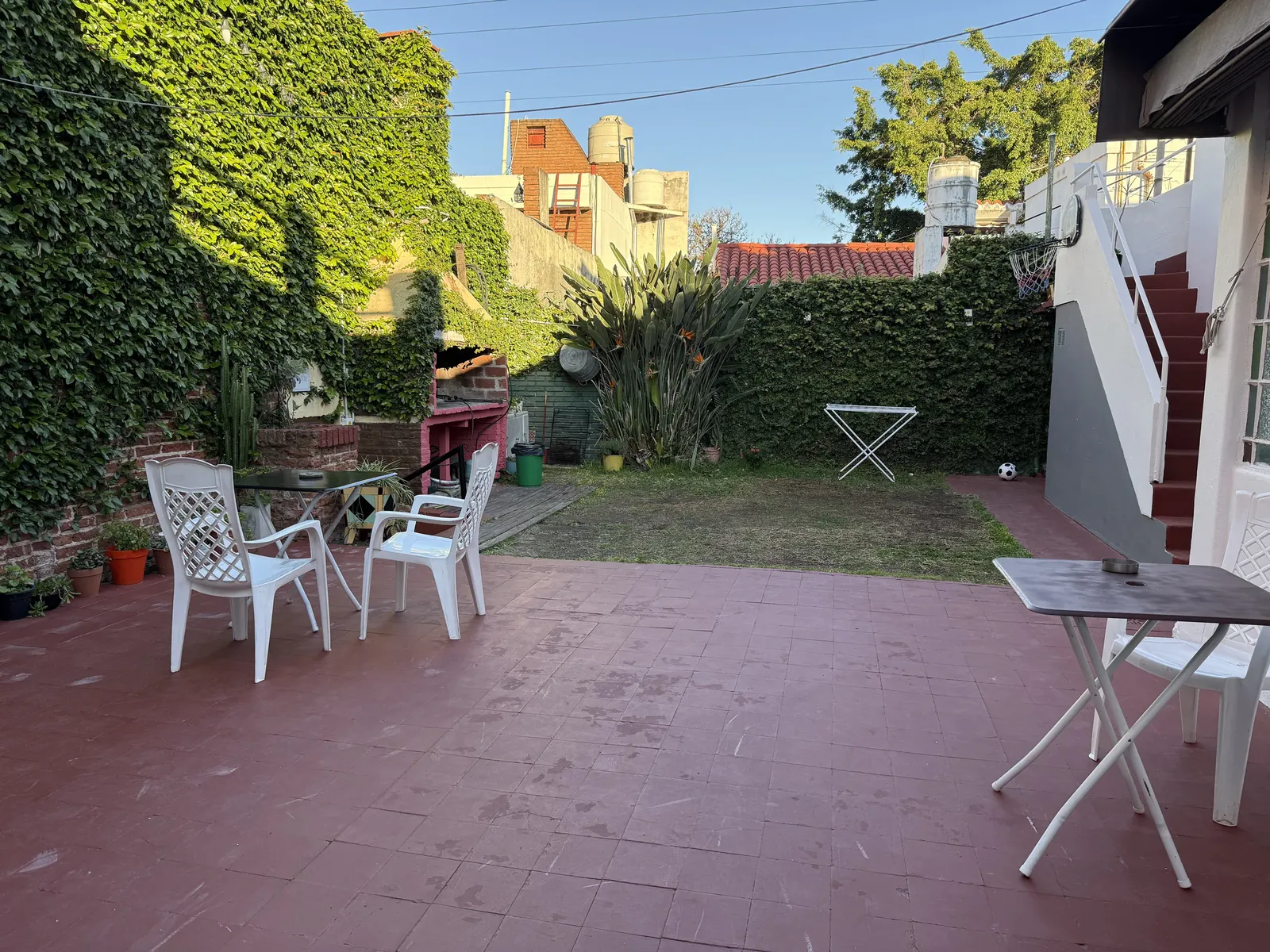 Patio amplio con mesas, sillas, enredadera y jardín al fondo