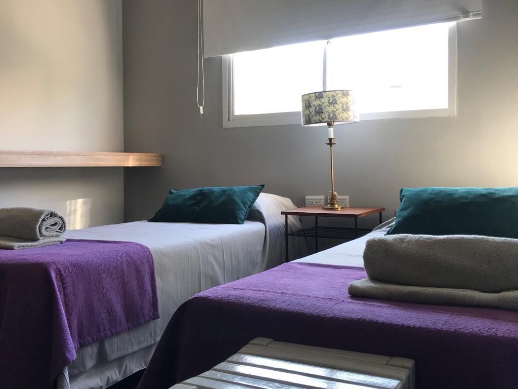 Habitación del dúplex con dos camas, almohadones verdes, toallas y lámpara sobre la mesa de luz