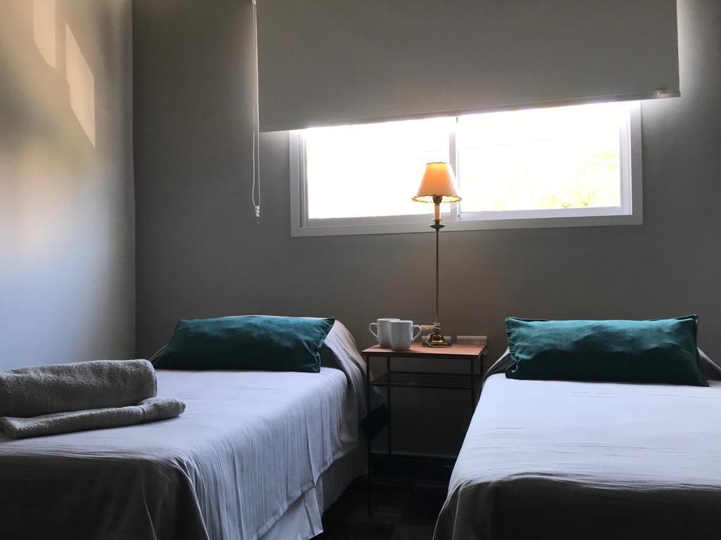 Habitación del dúplex con dos camas, almohadones verdes y lámpara encendida junto a la ventana