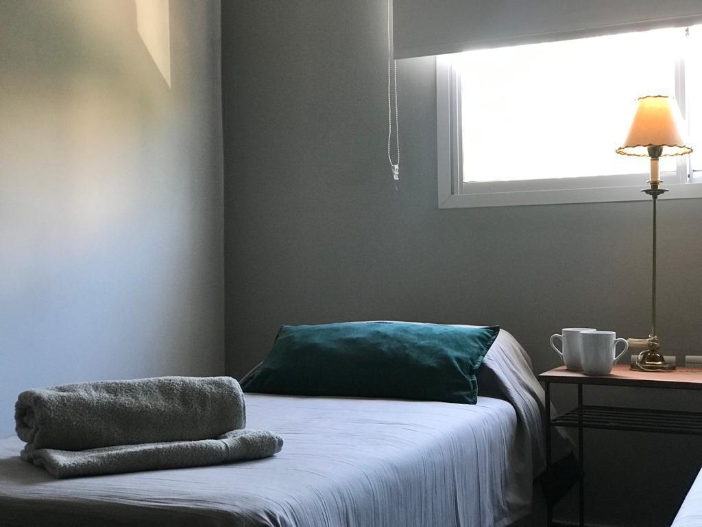 Cama individual del dúplex con almohadón verde, toallas y mesa de luz con lámpara