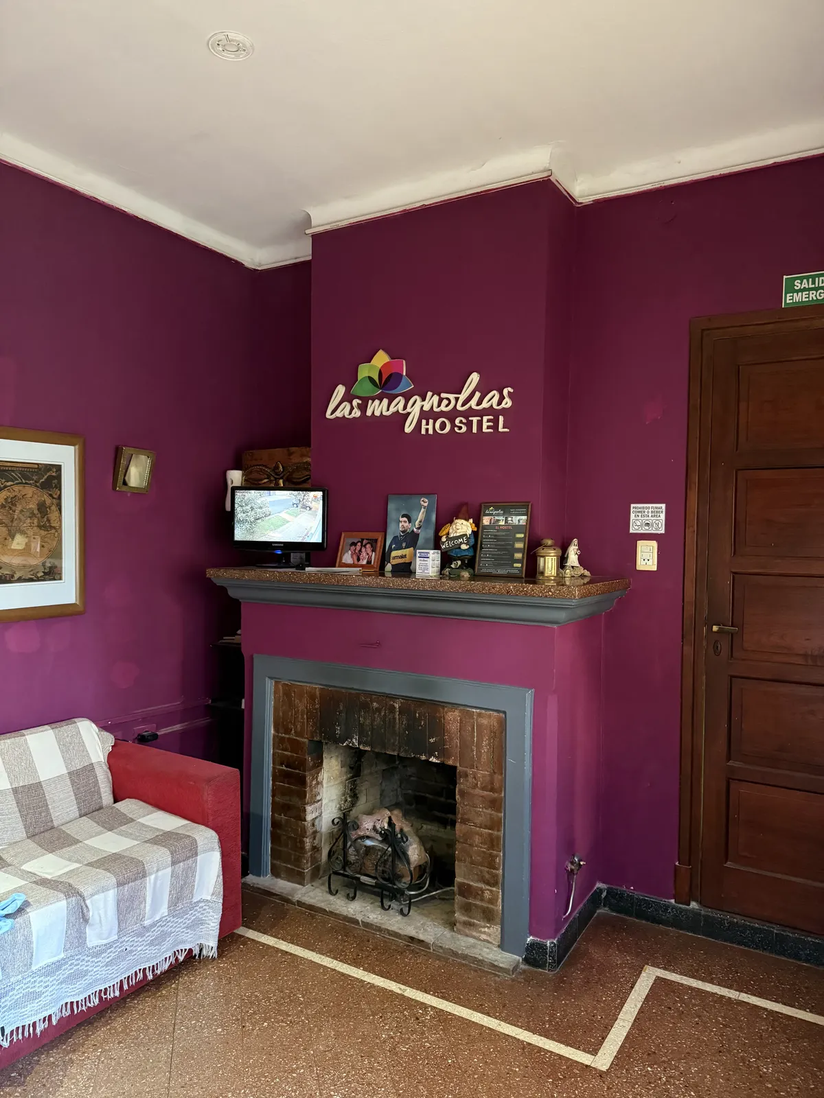 Sala de estar con hogar a leña y el cartel de Las Magnolias Hostel en la pared fucsia